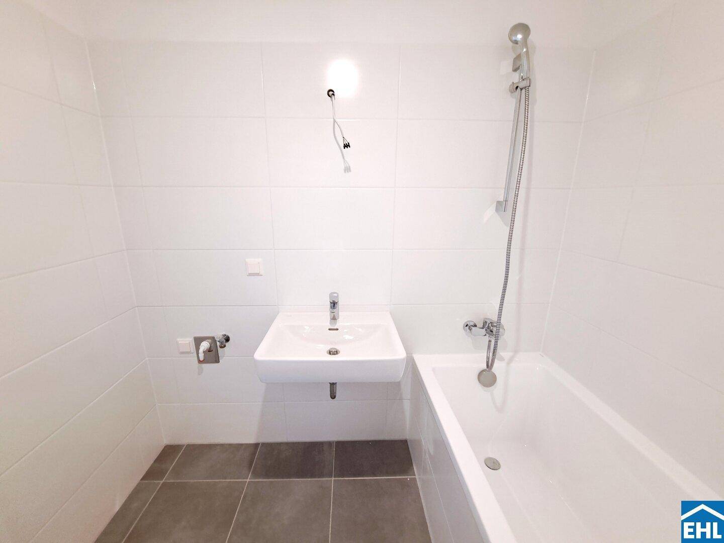 Modernes Badezimmer mit weißer Badewanne, Waschbecken und großen weißen Fliesen.
