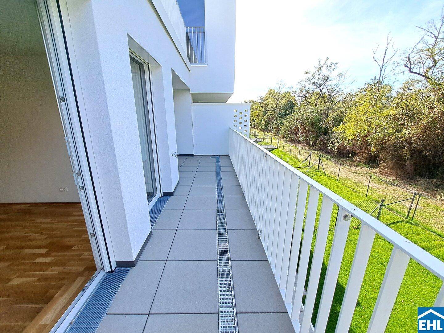 Langer, moderner Balkon mit Fliesenboden und Blick ins Grüne, ideal zum Entspannen.
