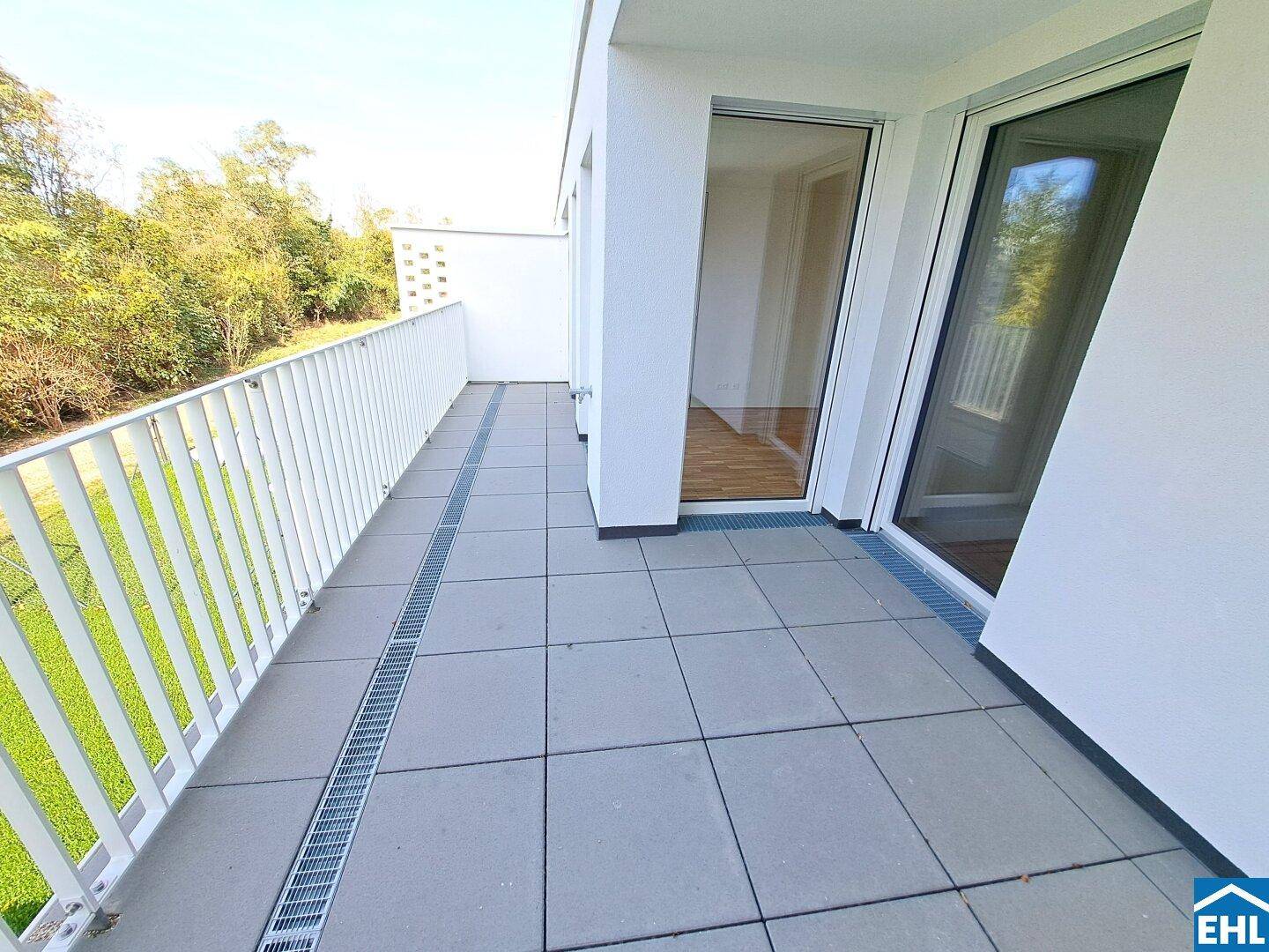 Heller Balkon mit modernem Fliesenboden und Zugang zu Innenräumen, umgeben von Natur.