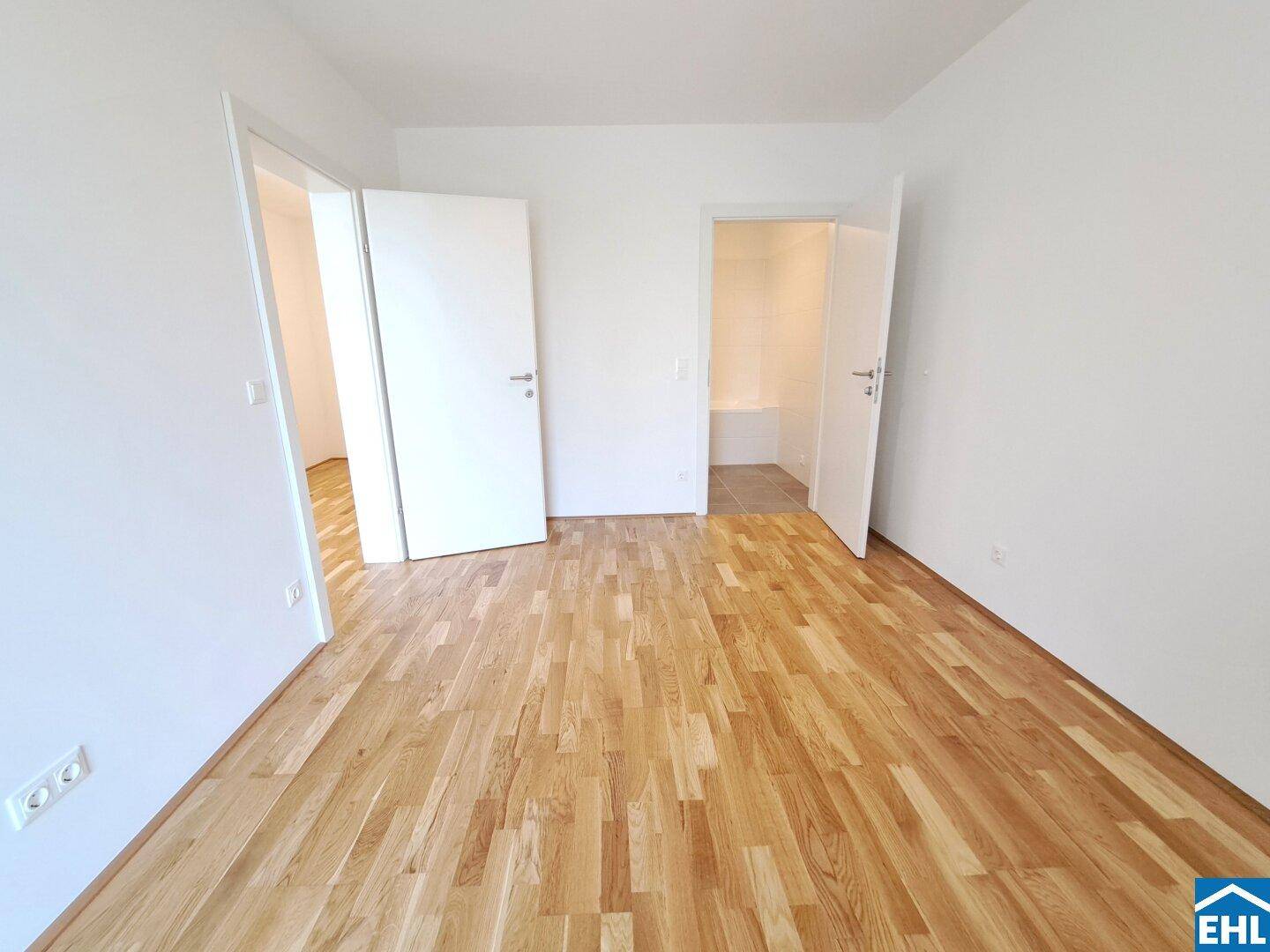 Helles Schlafzimmer mit Parkettboden und Zugang zu einem weiteren Raum und Badezimmer.