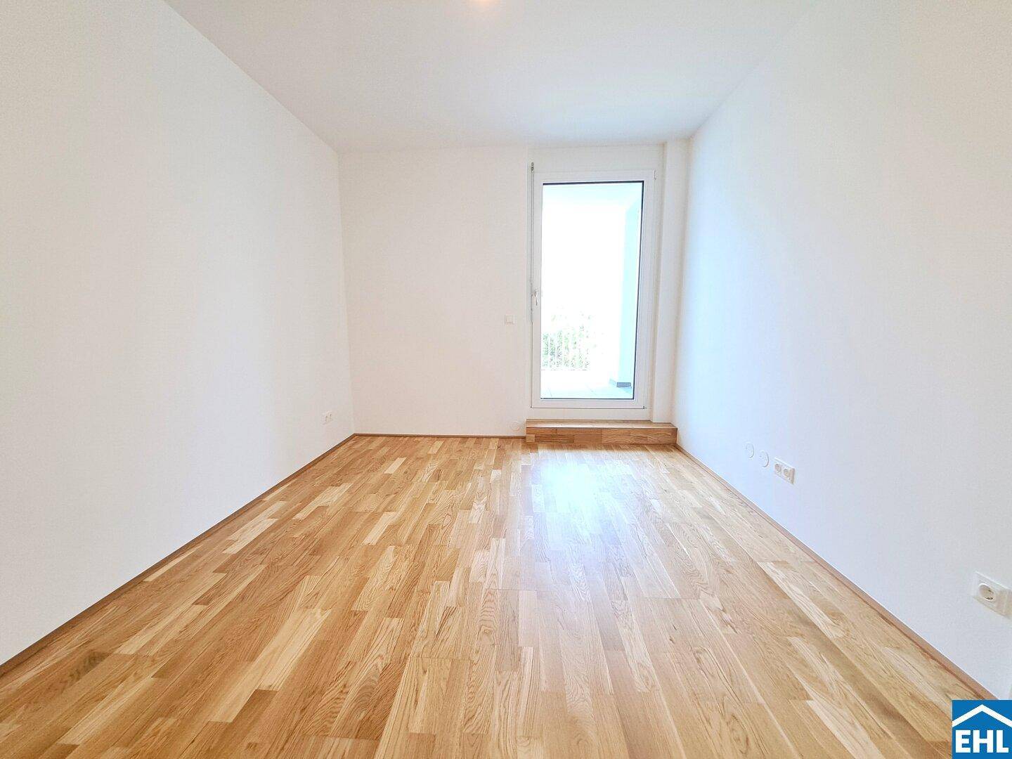 Lichtdurchfluteter Raum mit Holzboden und Zugang zu einem Außenbereich durch eine große Tür.