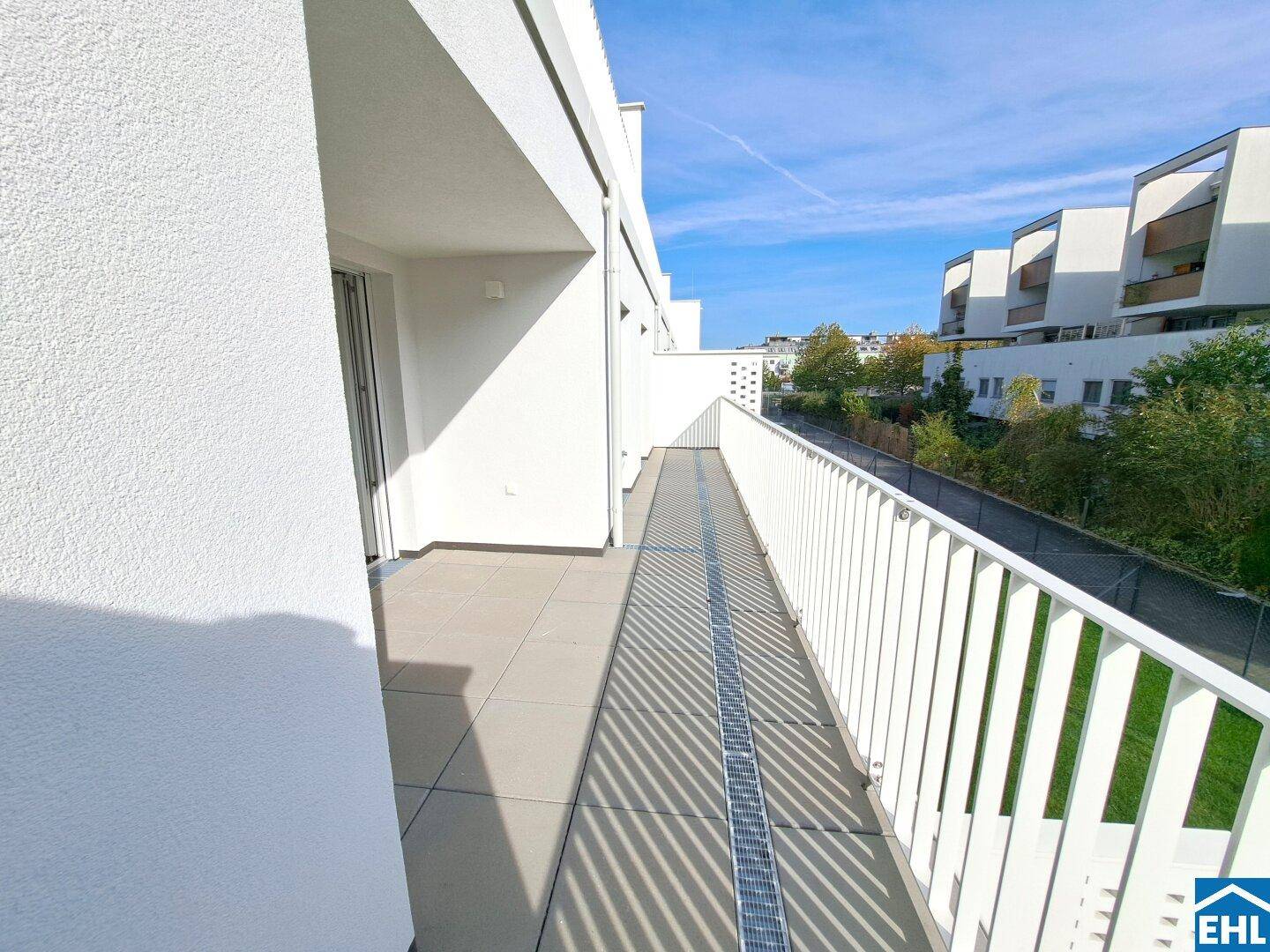 Langer, gefliester Balkon mit Metallgeländer und Blick auf die Umgebung.