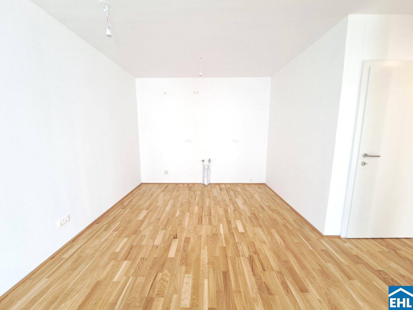 Leerer Küchenbereich mit Anschlüssen für eine moderne Einbauküche und hellem Parkettboden.