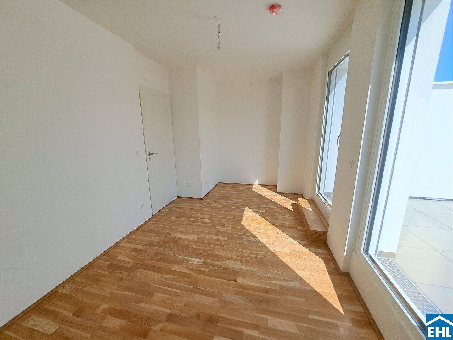 Unmöbliertes Zimmer mit Holzboden und Zugang zu einem Außenbereich durch große Fenstertüren.