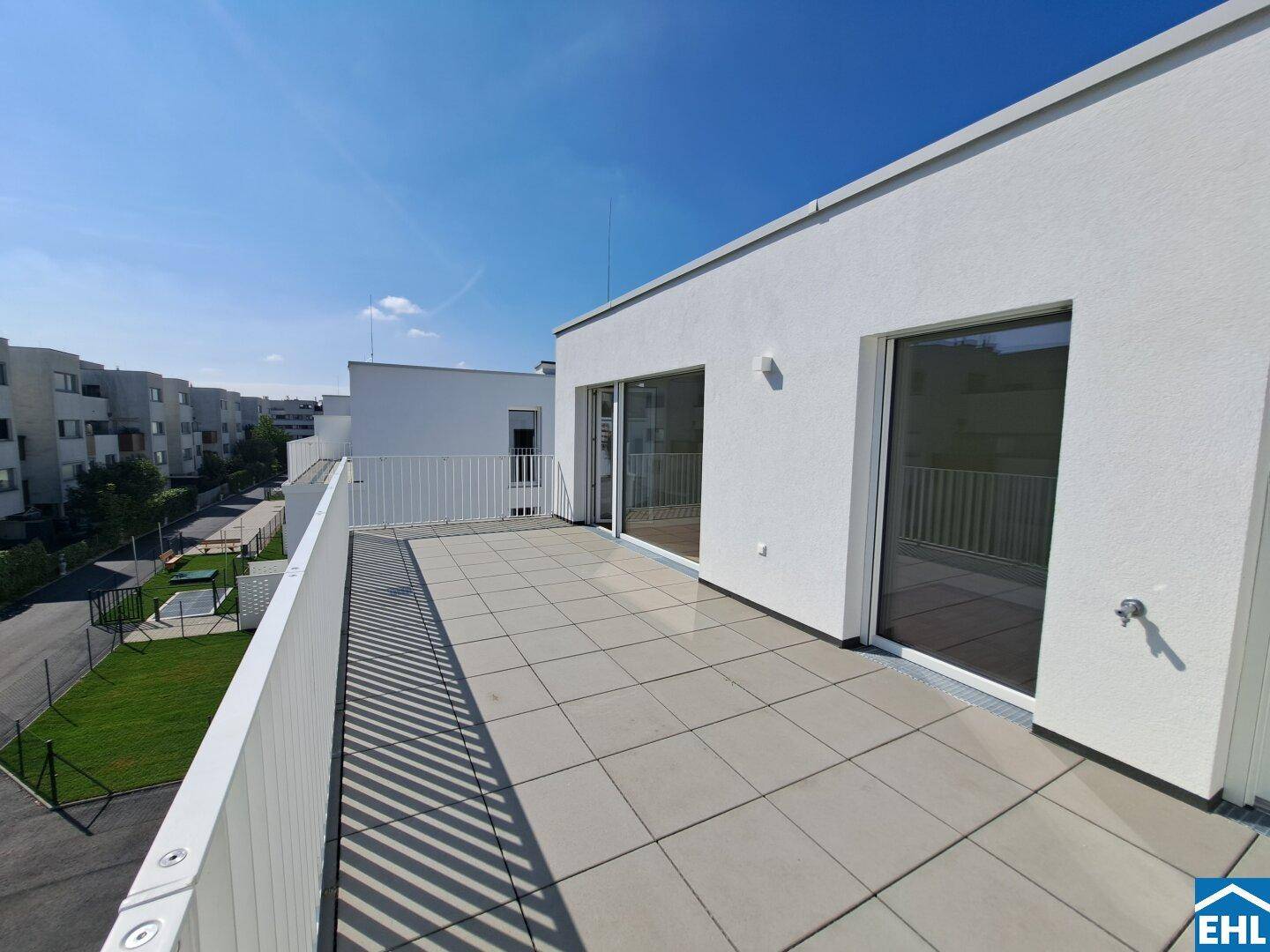 Weitläufige Dachterrasse mit Blick auf die umliegenden modernen Wohngebäude und Grünflächen.