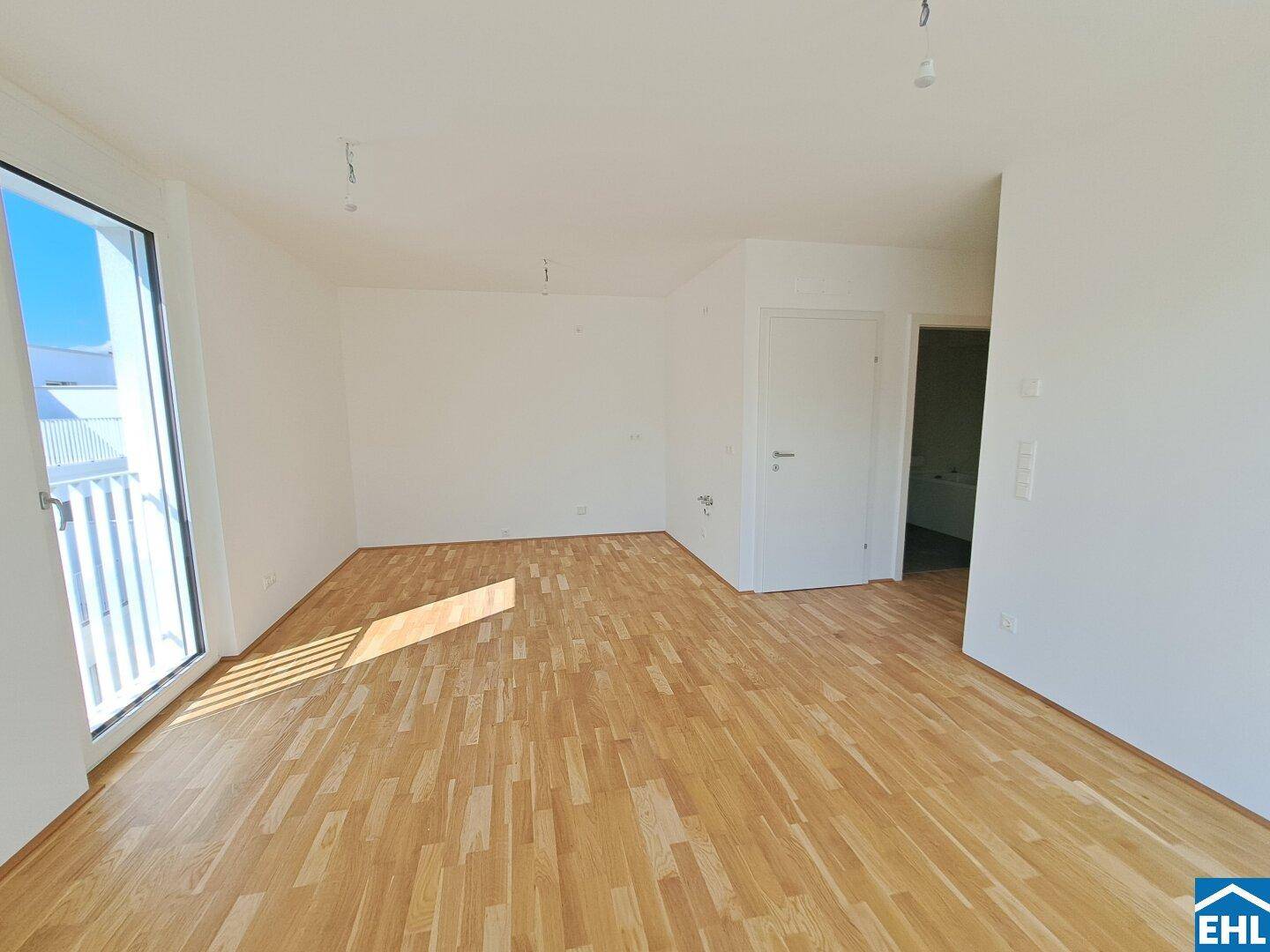 Geräumiger, unmöblierter Wohnbereich mit hellem Holzboden und weiß gestrichenen Wänden.