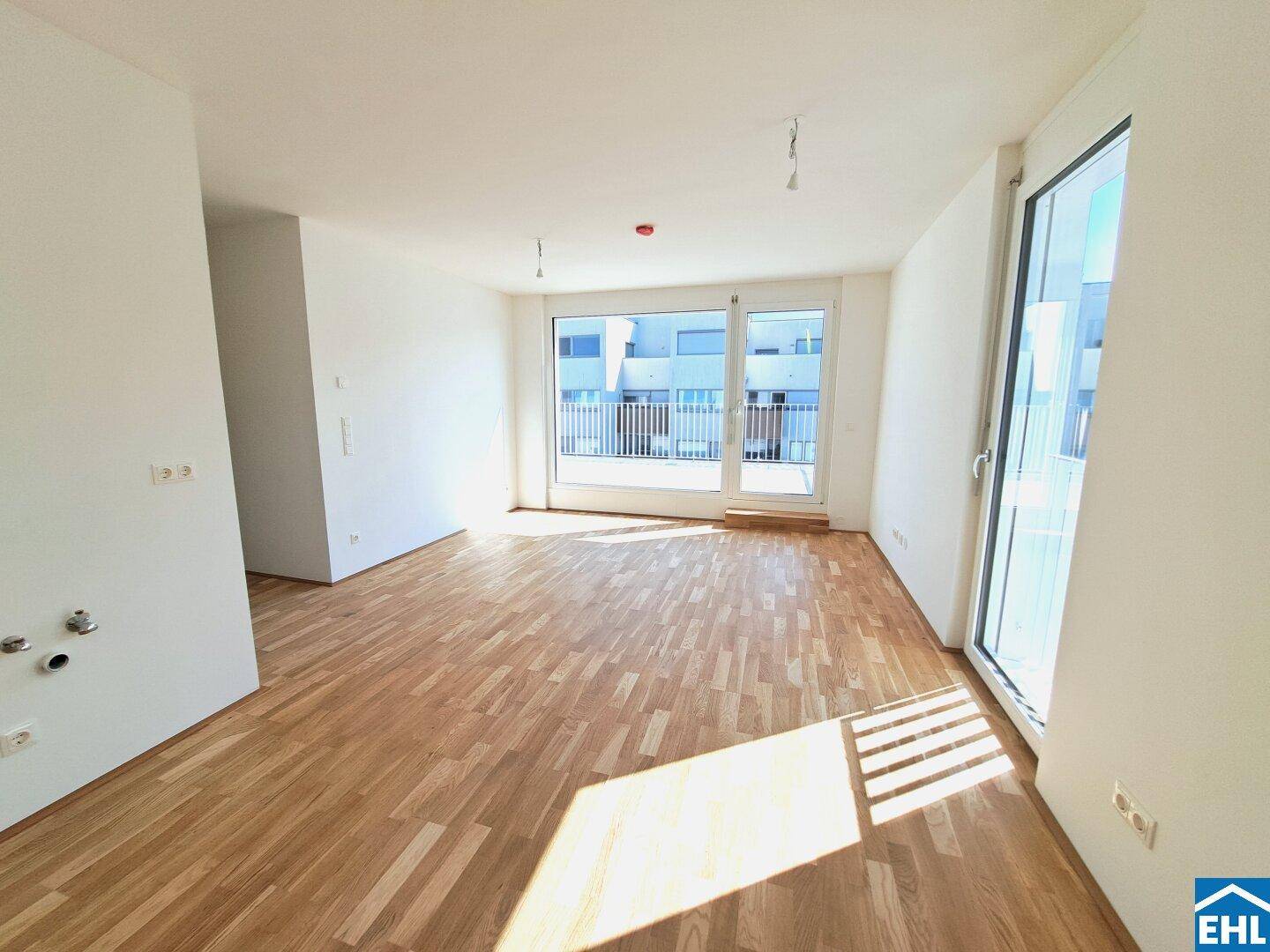 Heller, leerer Wohnraum mit Holzboden und Zugang zu einem Balkon oder einer Terrasse.
