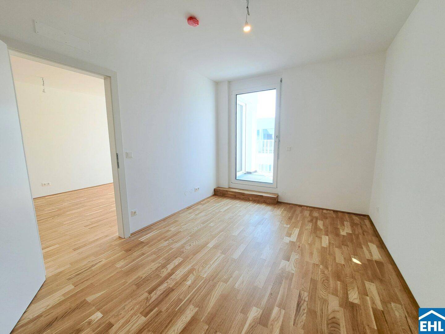 Helles Schlafzimmer mit Parkettboden und großem Fenster, das viel Tageslicht hereinlässt.
