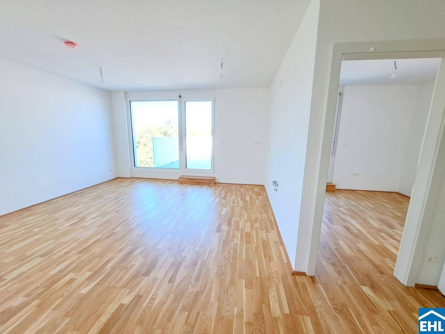 Helles, leeres Zimmer mit Parkettboden und großem Fenster, das viel Tageslicht hereinlässt.