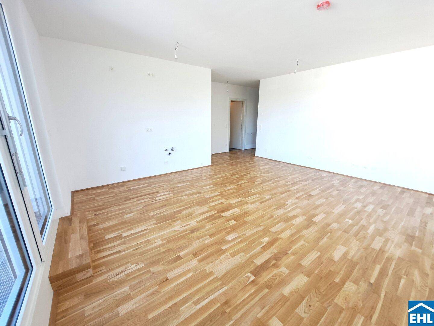 Lichtdurchfluteter, leerer Raum mit Parkettboden und großem Fenster, das den Blick nach draußen freigibt.
