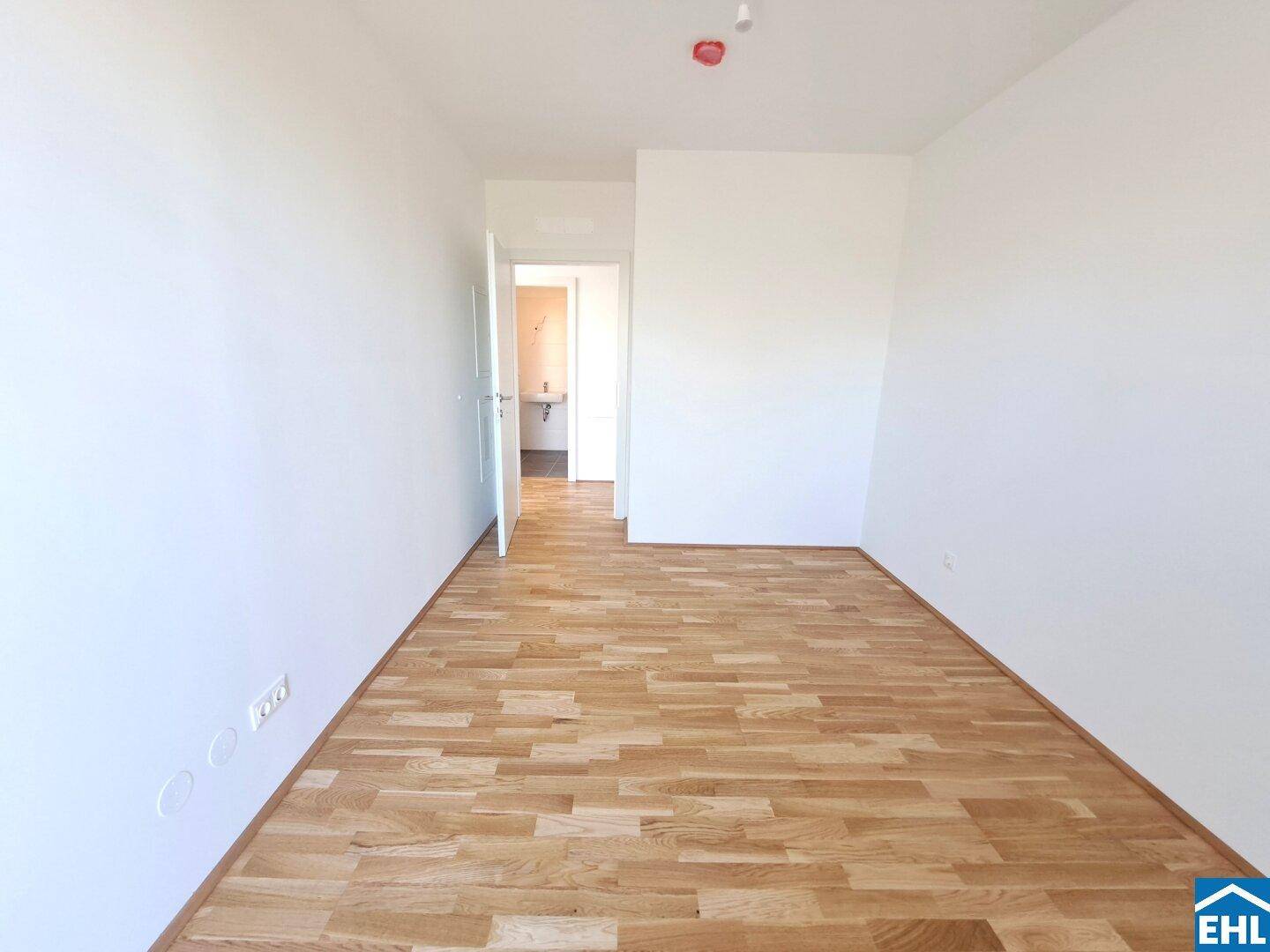 Leeres Zimmer mit Parkettboden und Zugang zu einem Badezimmer, ideal als Schlaf- oder Gästezimmer.