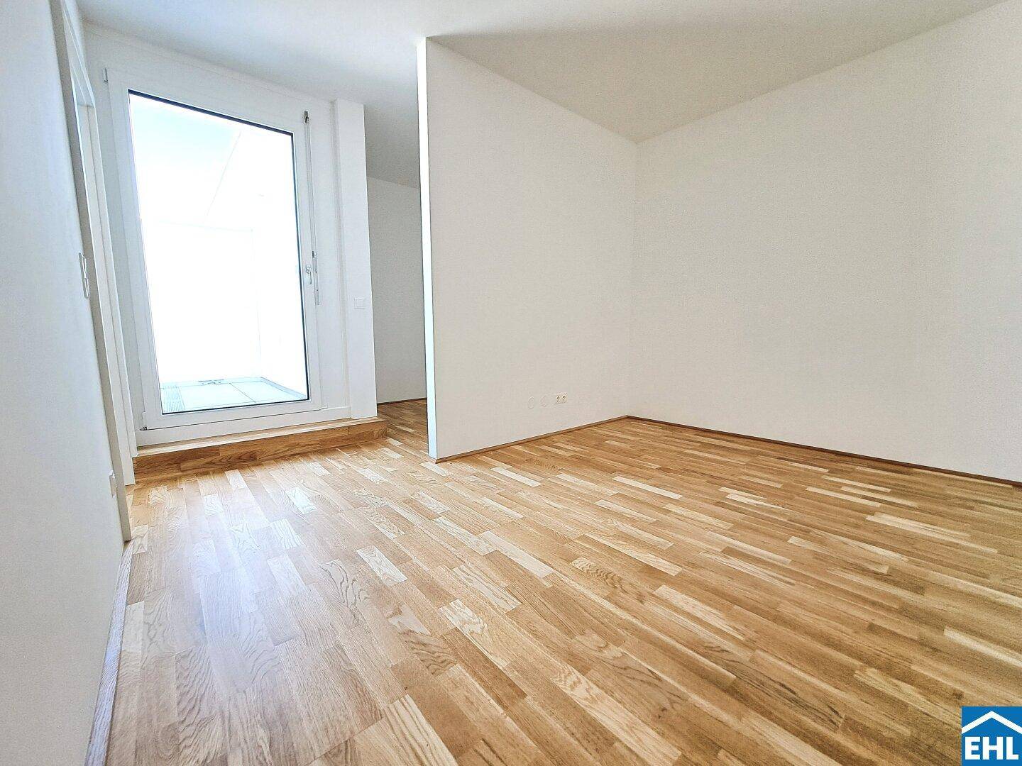Heller Raum mit Parkettboden und Zugang zu einem Balkon oder einer kleinen Terrasse.