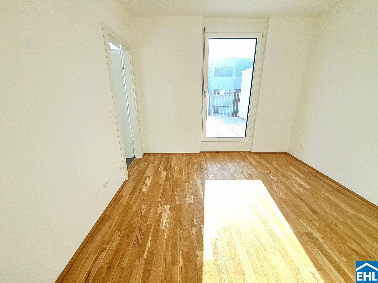 Helles Schlafzimmer mit Parkettboden und großem Fenster mit Blick nach draußen.