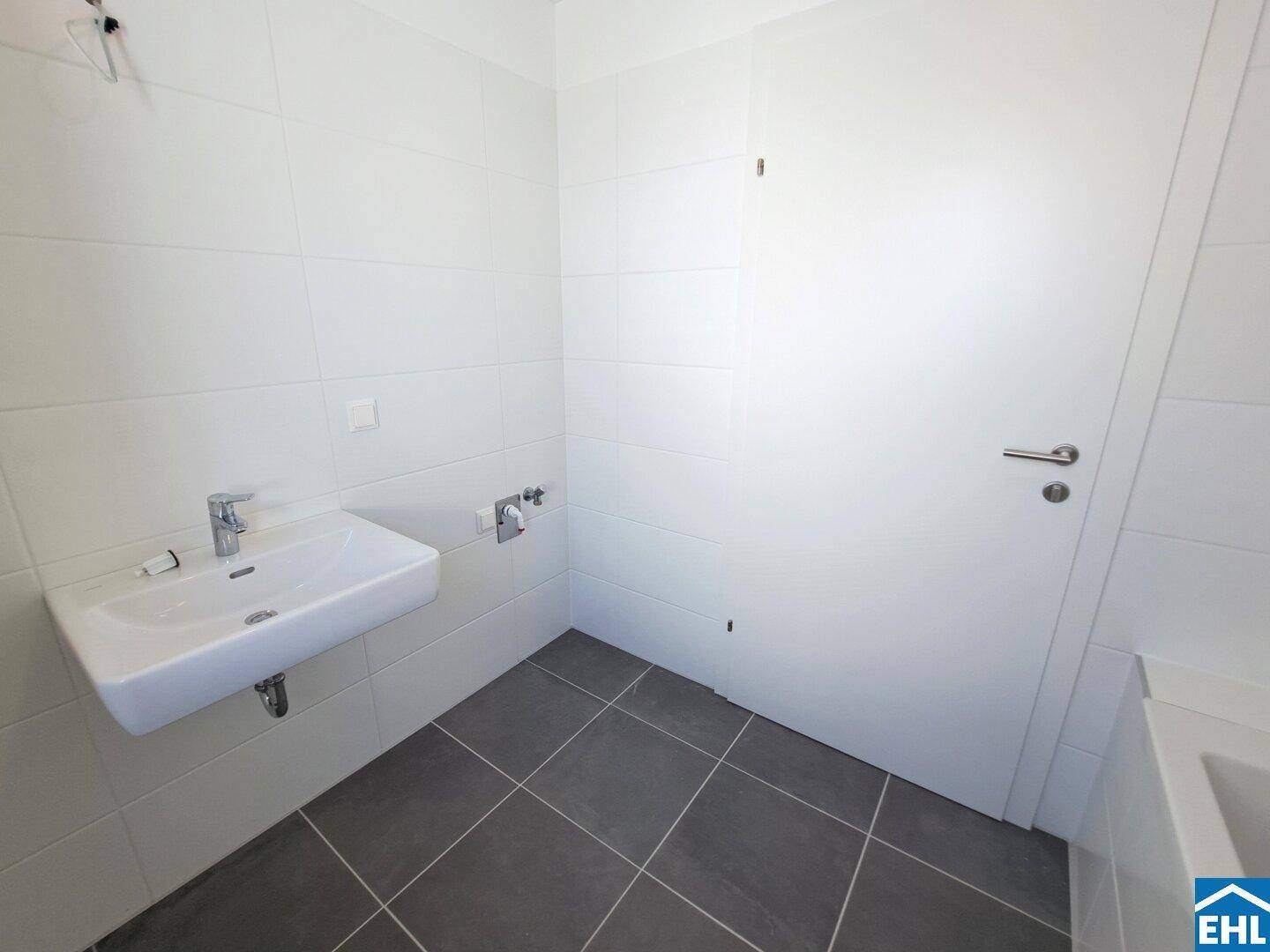 Modernes Badezimmer mit weißen Wandfliesen, dunklem Boden und wandhängendem Waschbecken.
