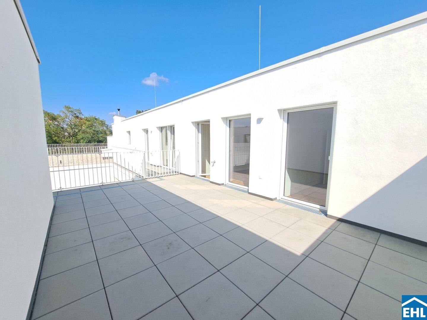 Geräumige Dachterrasse mit hellen Fliesen und Zugang zu mehreren Innenräumen.