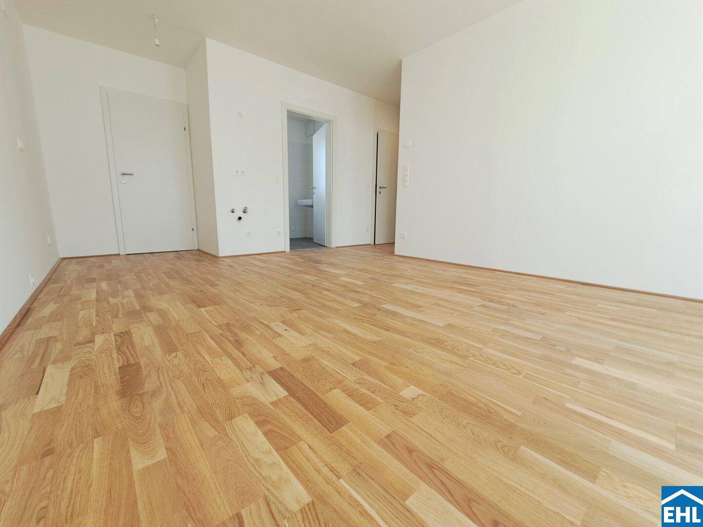 Leerer Raum mit hellem Parkettboden und weiß gestrichenen Wänden, Blick zum Bad.