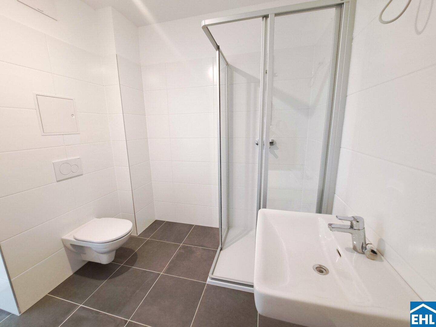 Modernes Badezimmer mit Dusche, WC und Waschbecken, ausgestattet mit weißen und grauen Fliesen.