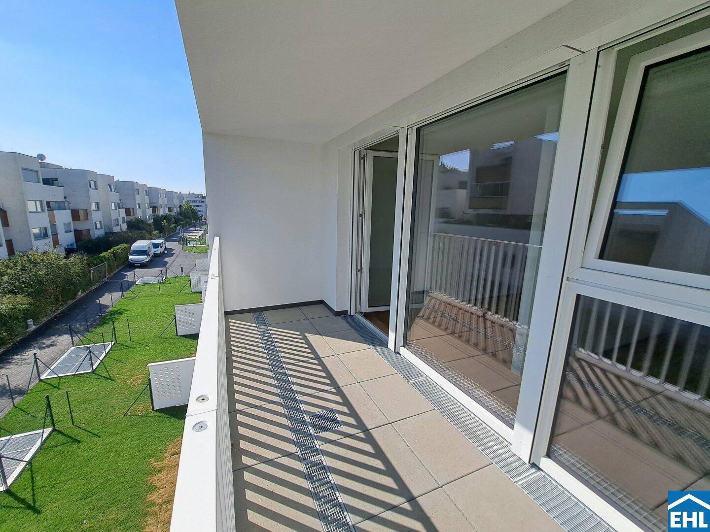 Geräumiger Balkon mit Fliesenboden und Blick auf die umliegenden Neubauten und Grünflächen.