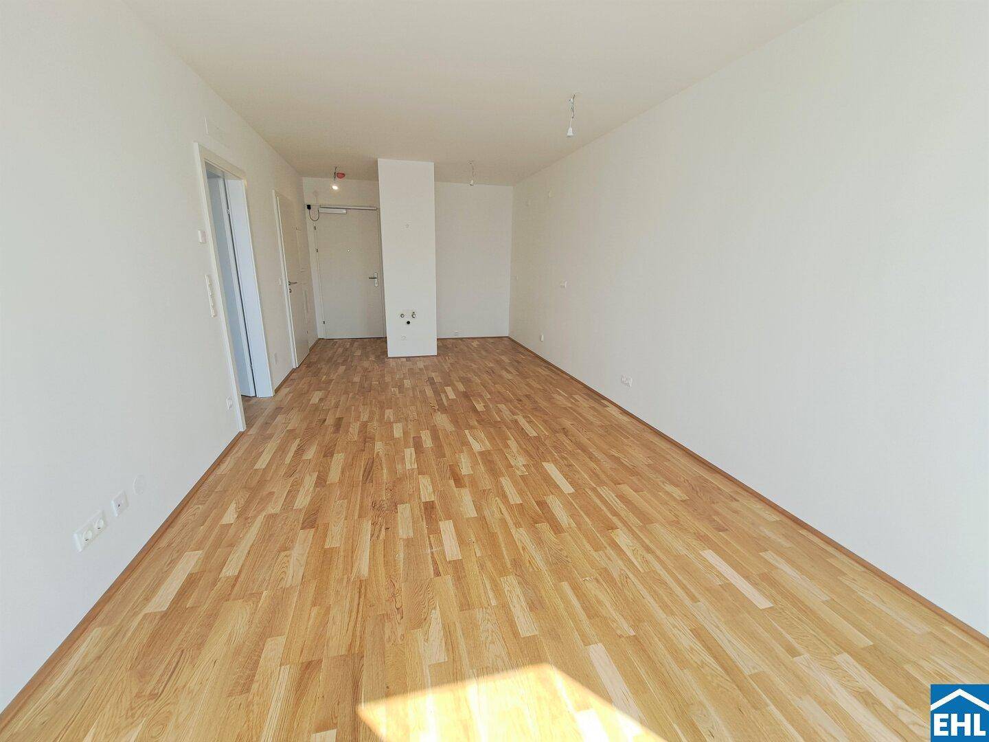 Geräumiges, leeres Zimmer mit hellem Parkettboden und weißen Wänden.