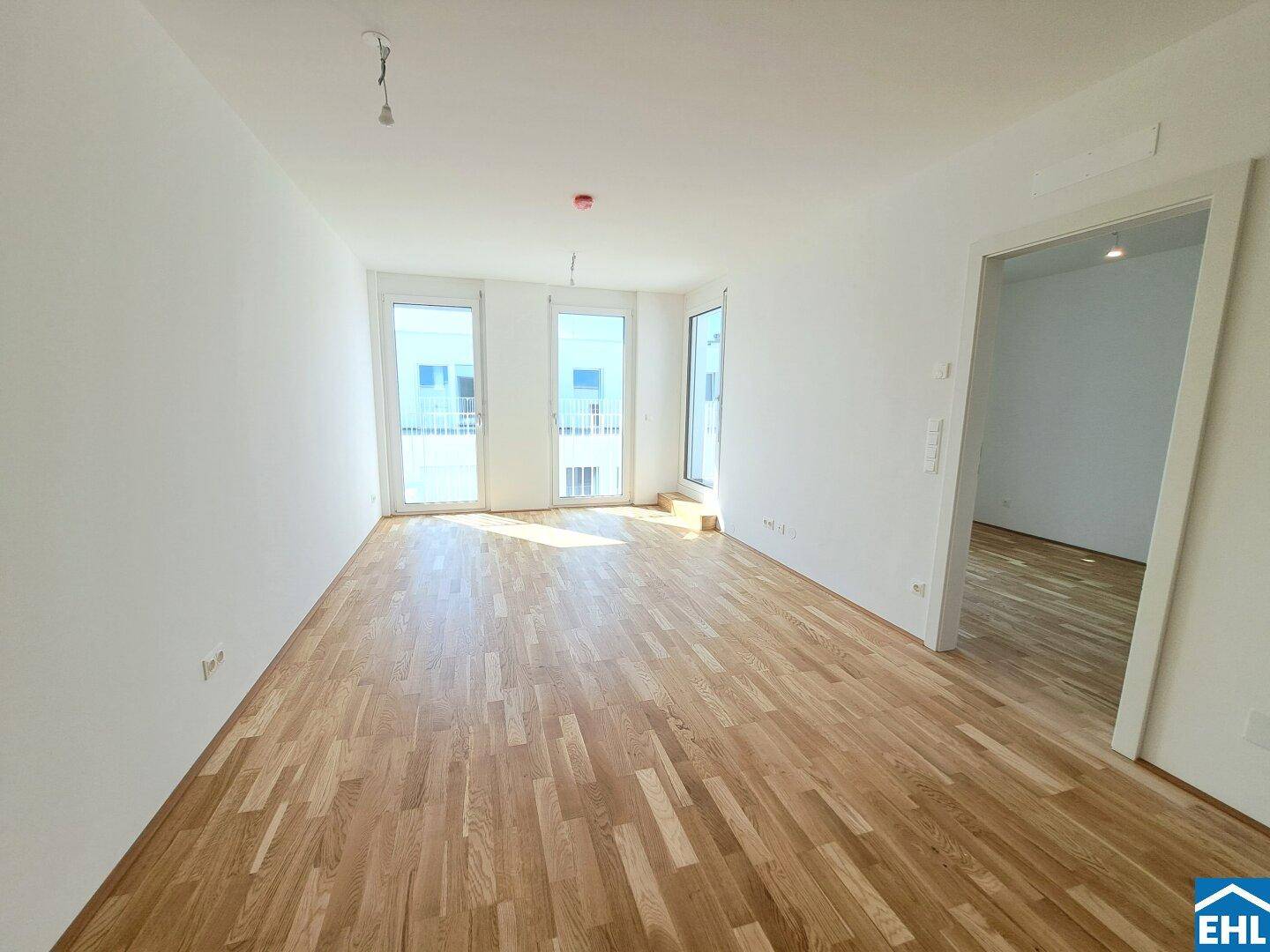 Lichtdurchflutetes Zimmer mit Parkettboden und mehreren Fenstertüren zum Außenbereich.