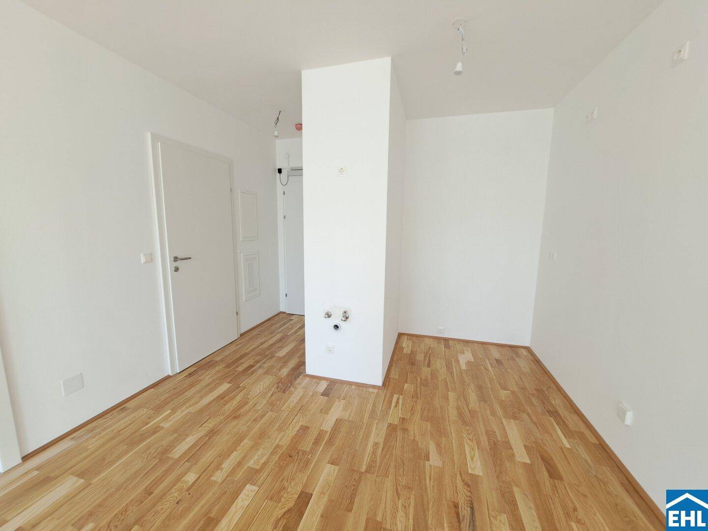Leerer Raum mit Parkettboden und einem Installationsschacht, bereit für die Kücheneinrichtung.