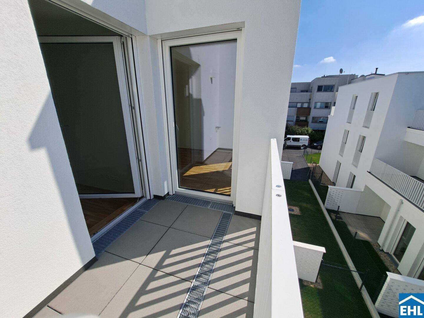 Heller Balkon mit Fliesenboden und Zugang zum Innenbereich, umgeben von moderner Architektur.