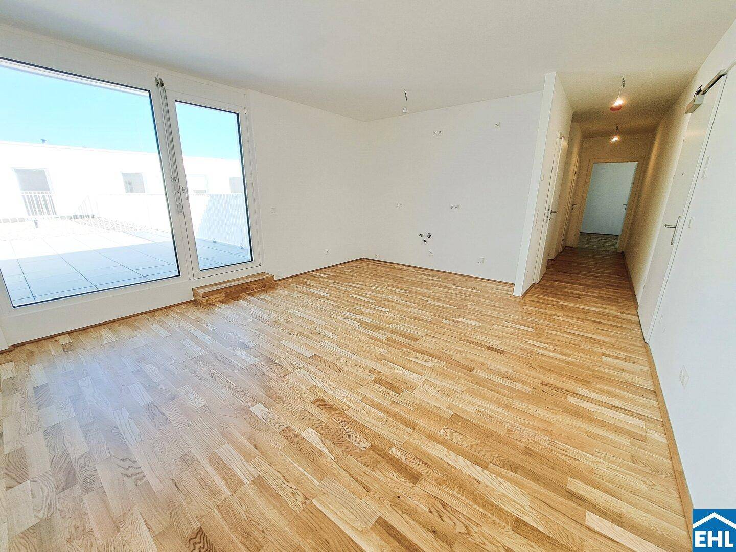 Lichtdurchflutetes Zimmer mit großen Fenstern, Parkettboden und Zugang zu einer weitläufigen Terrasse.