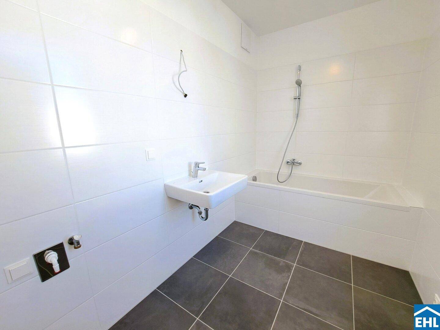 Modernes Badezimmer mit weißen Fliesen, dunklem Boden und Badewanne mit Duschfunktion.