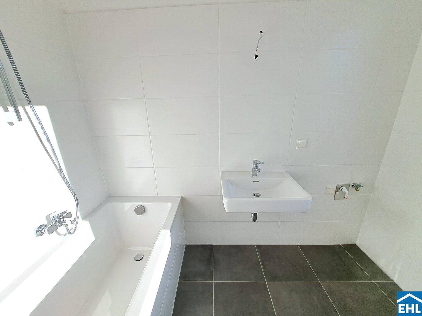 Helles Badezimmer mit Badewanne, Waschbecken und modernen Fliesen in Weiß und Grau.