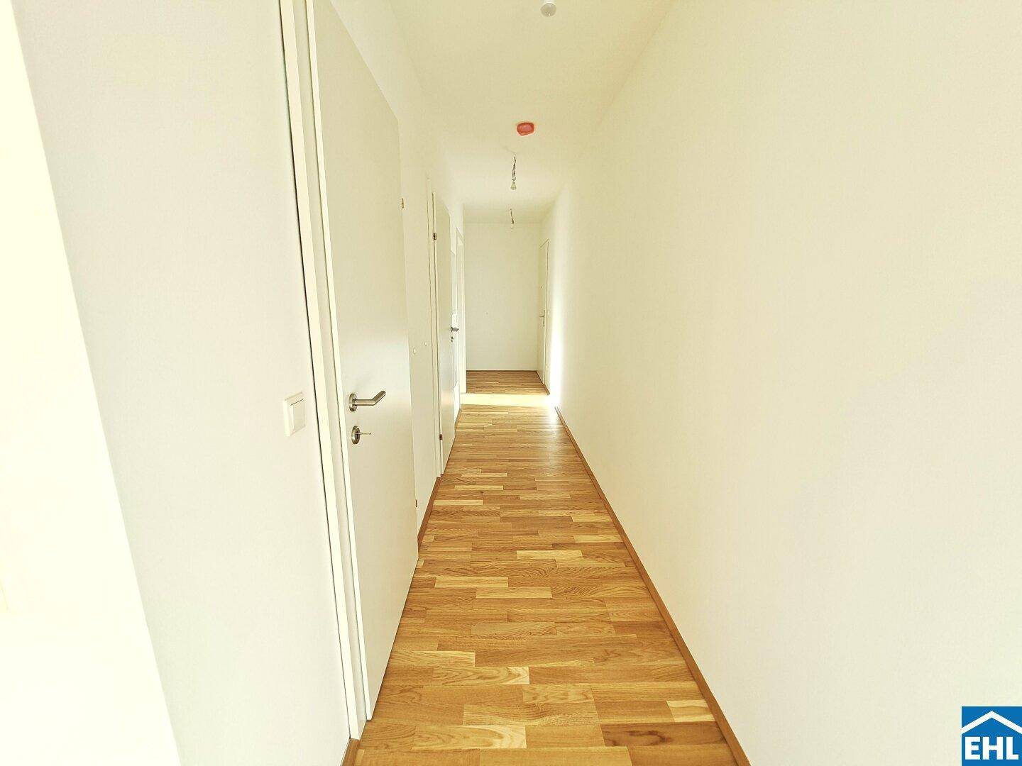 Langer, heller Flur mit Parkettboden, der zu verschiedenen Räumen der Wohnung führt.