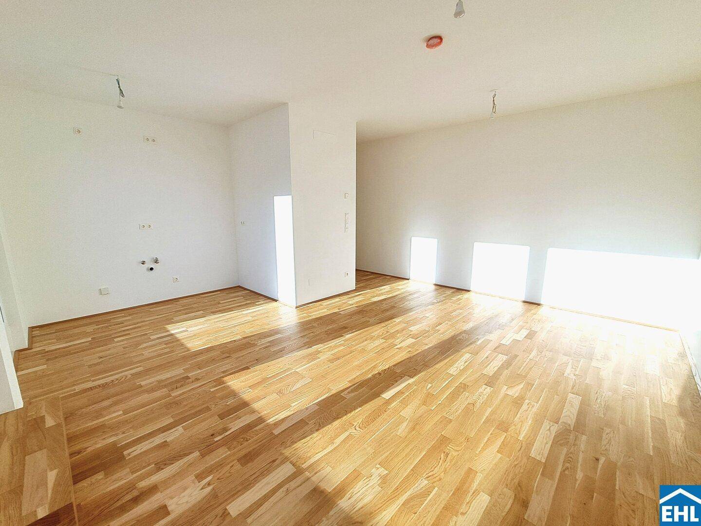 Geräumiger, unmöblierter Küchenbereich mit hellem Parkettboden und viel Tageslicht.