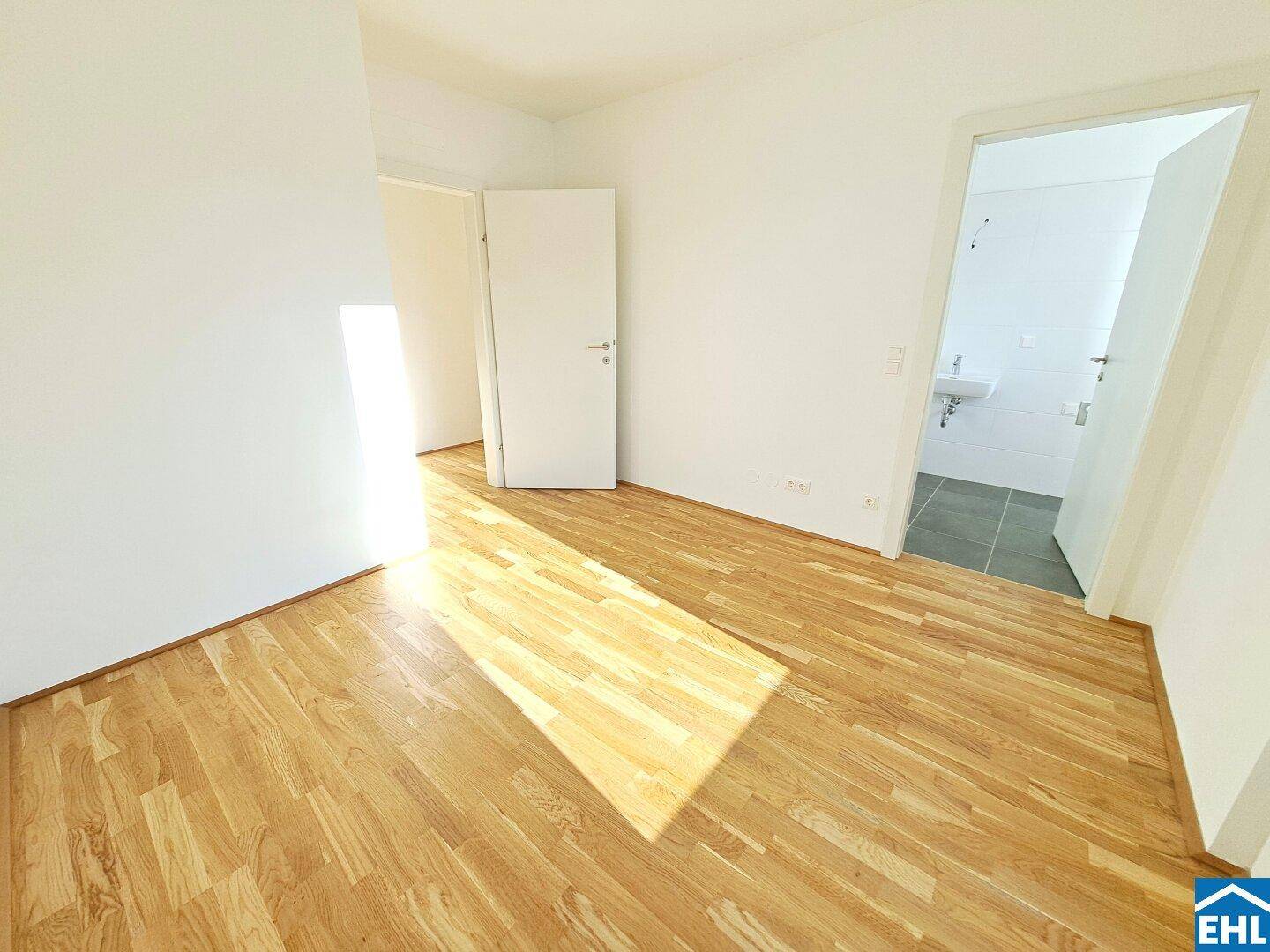 Leeres Schlafzimmer mit Parkettboden und direktem Zugang zu einem angrenzenden Badezimmer.