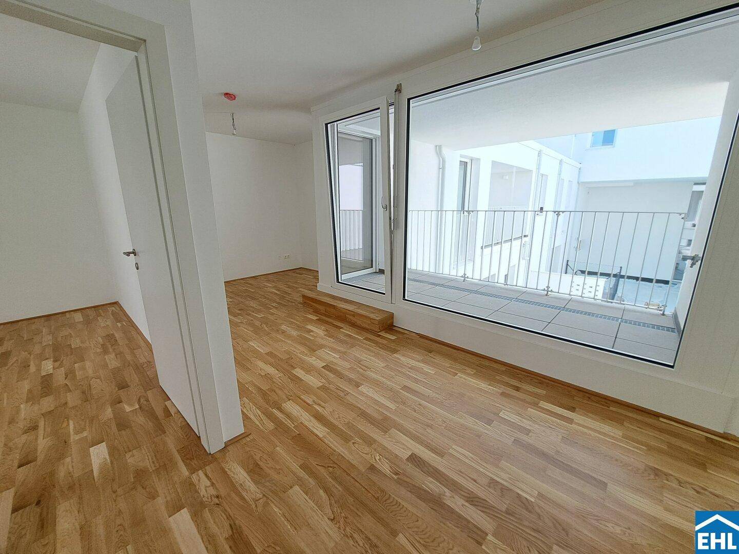 Geräumiger Wohnbereich mit Holzboden und Zugang zu einem Balkon, der viel Licht bietet.