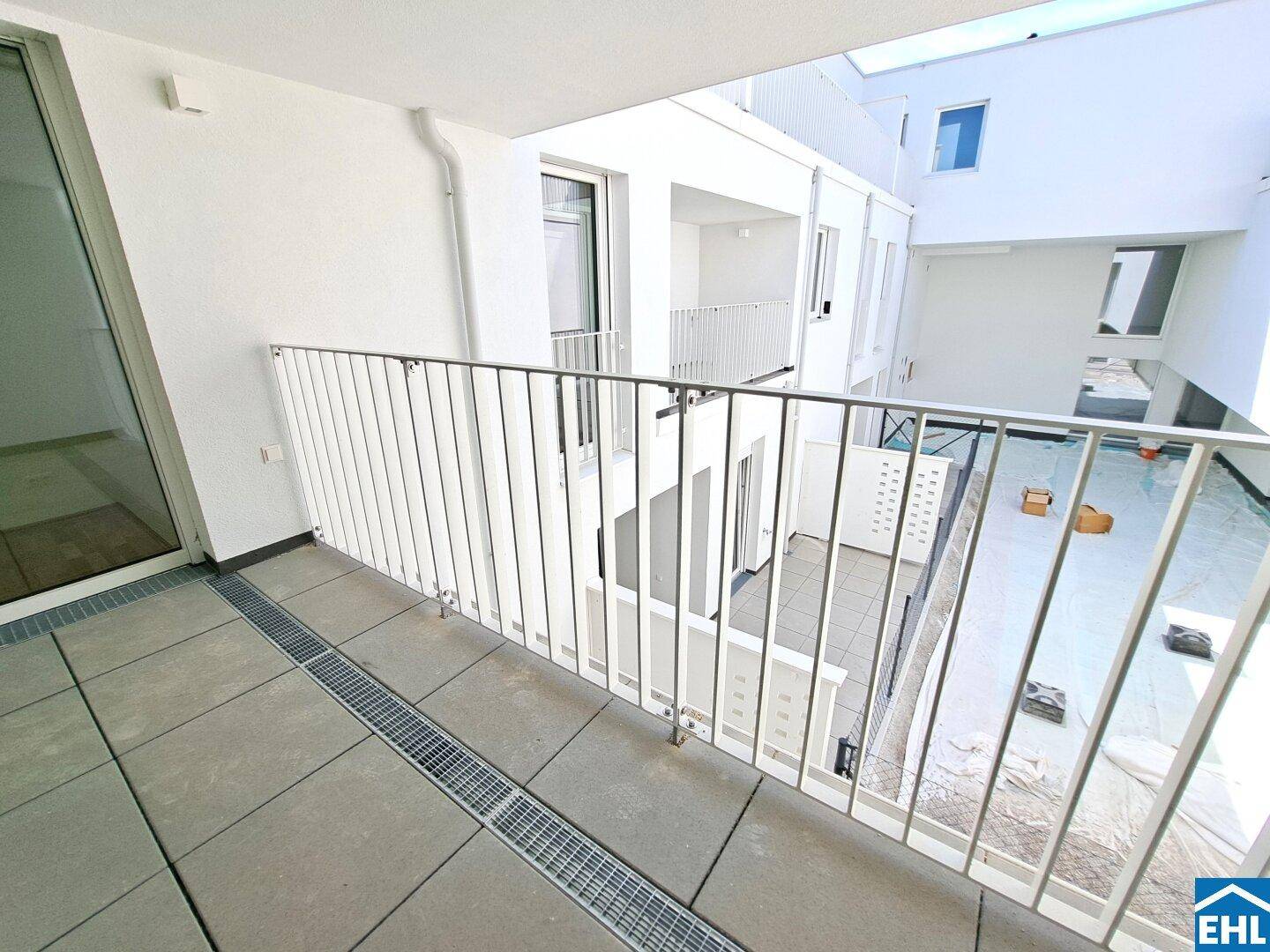 Geräumiger Balkon mit Fliesenboden und Blick auf den Innenhof des Neubaus.