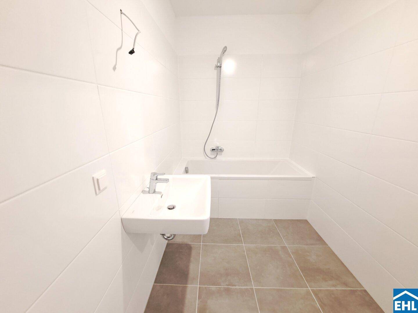 Modernes Badezimmer mit weißen Fliesen, Badewanne und integrierter Dusche sowie einem Waschbecken.