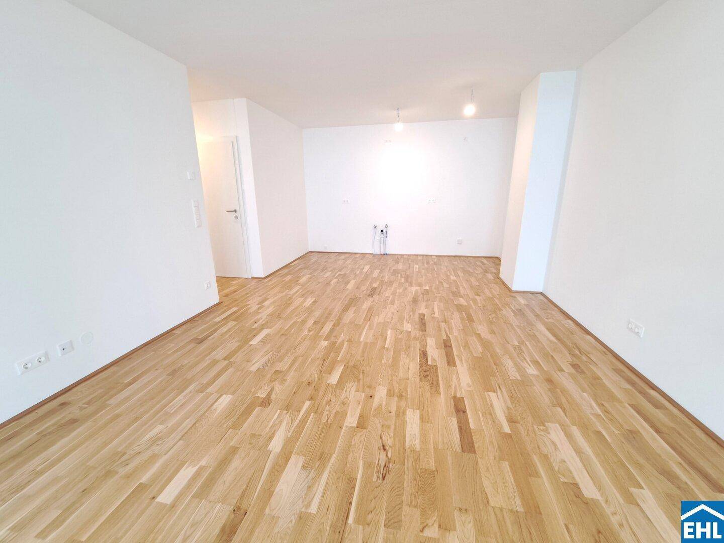 Leerer Küchenbereich mit Anschlüssen für eine Einbauküche und neuem Holzparkettboden.