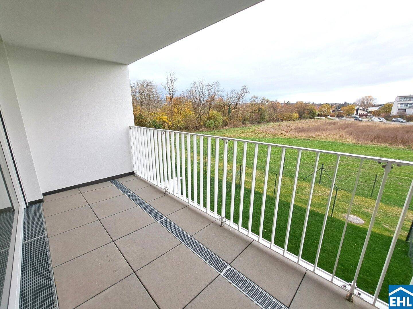 Heller Balkon mit Fliesenboden und Blick auf eine grüne Wiese und die Umgebung.