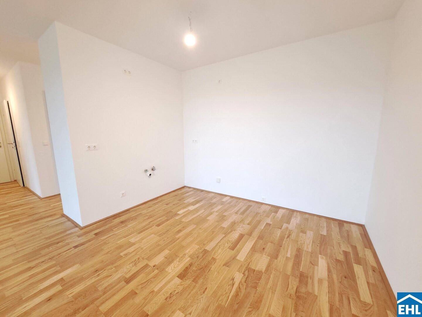 Leerer Raum mit Parkettboden und Anschlüssen für eine Küche, bereit für den Einbau.
