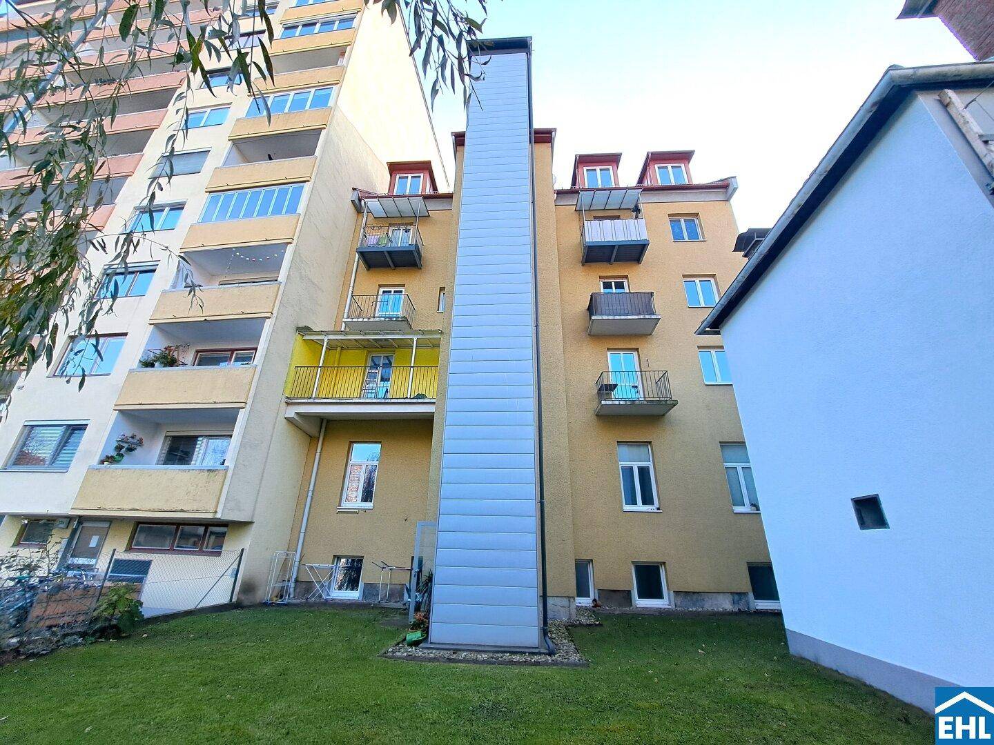 Rückansicht eines Gebäudes mit neu angebautem Aufzugsschacht und Balkonen.