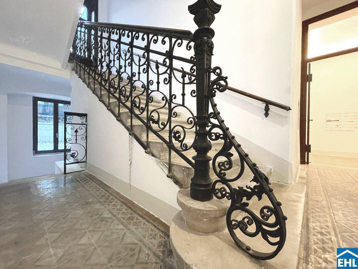 Elegantes Treppenhaus mit geschwungenem schmiedeeisernem Geländer und Steinstufen.