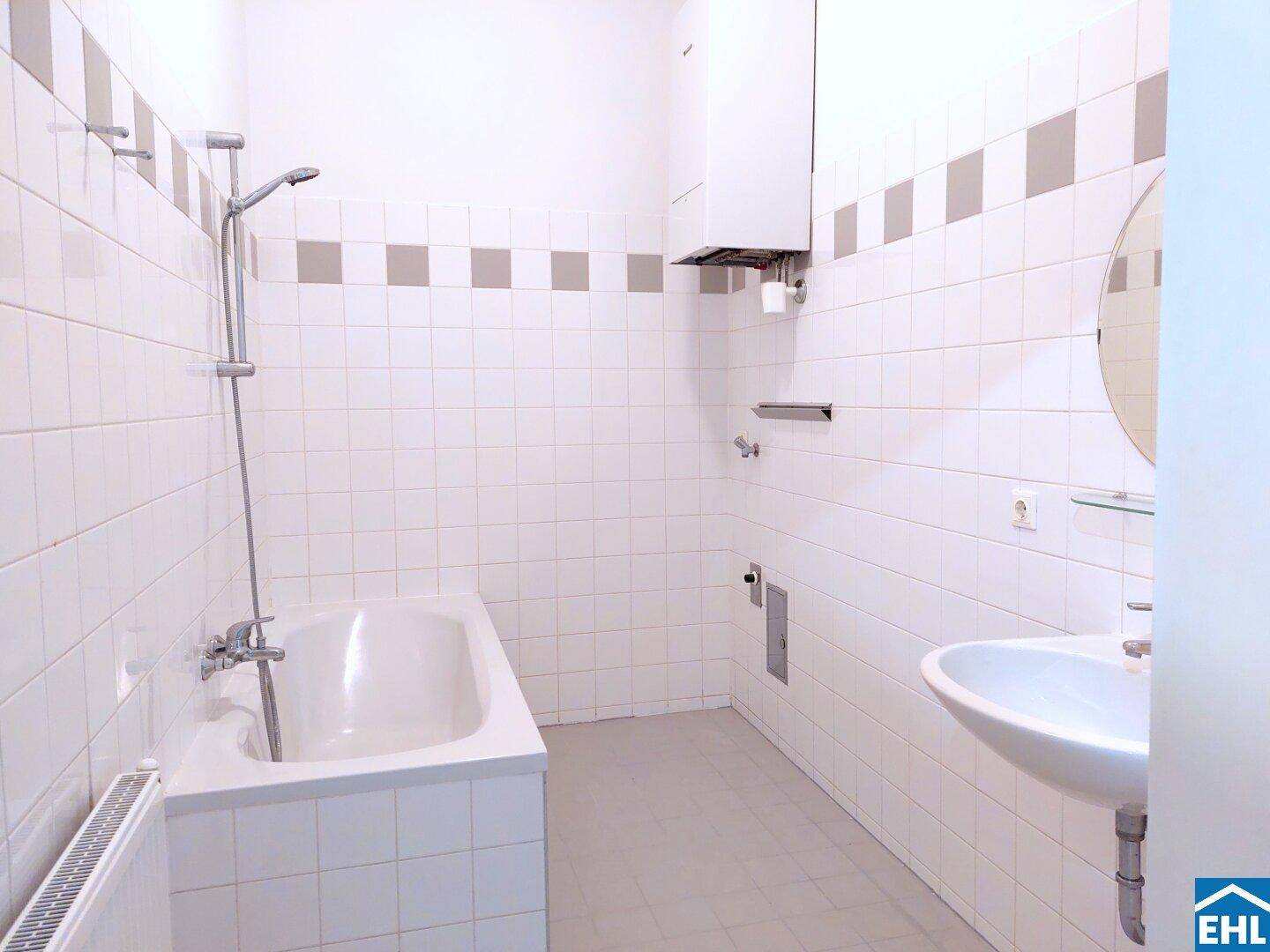 Gefliestes Badezimmer mit Badewanne, Waschbecken und Gastherme an der Wand.