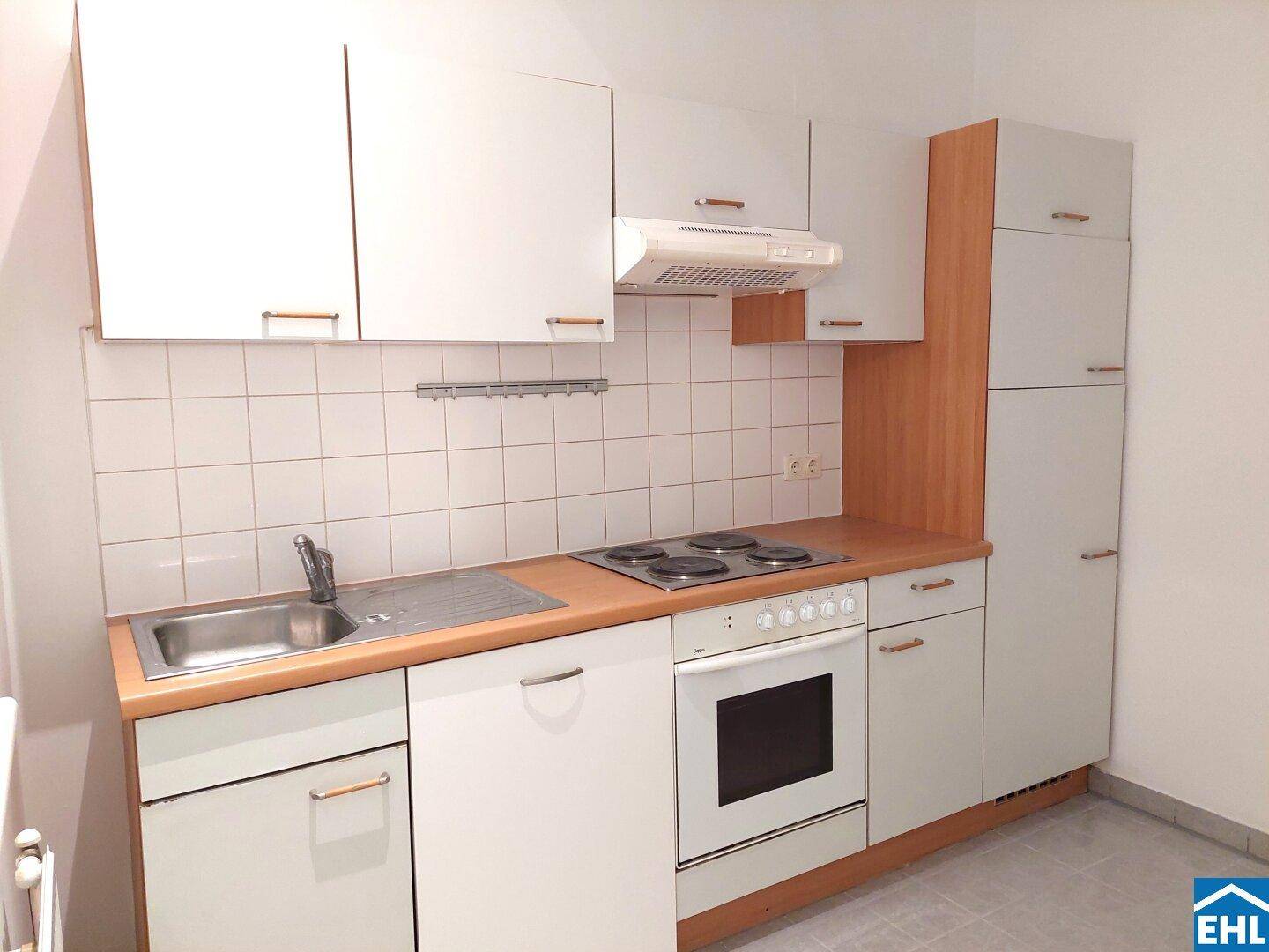 Funktionale Einbauküche mit weißen Schränken, Holz-Arbeitsplatte und Elektroherd.
