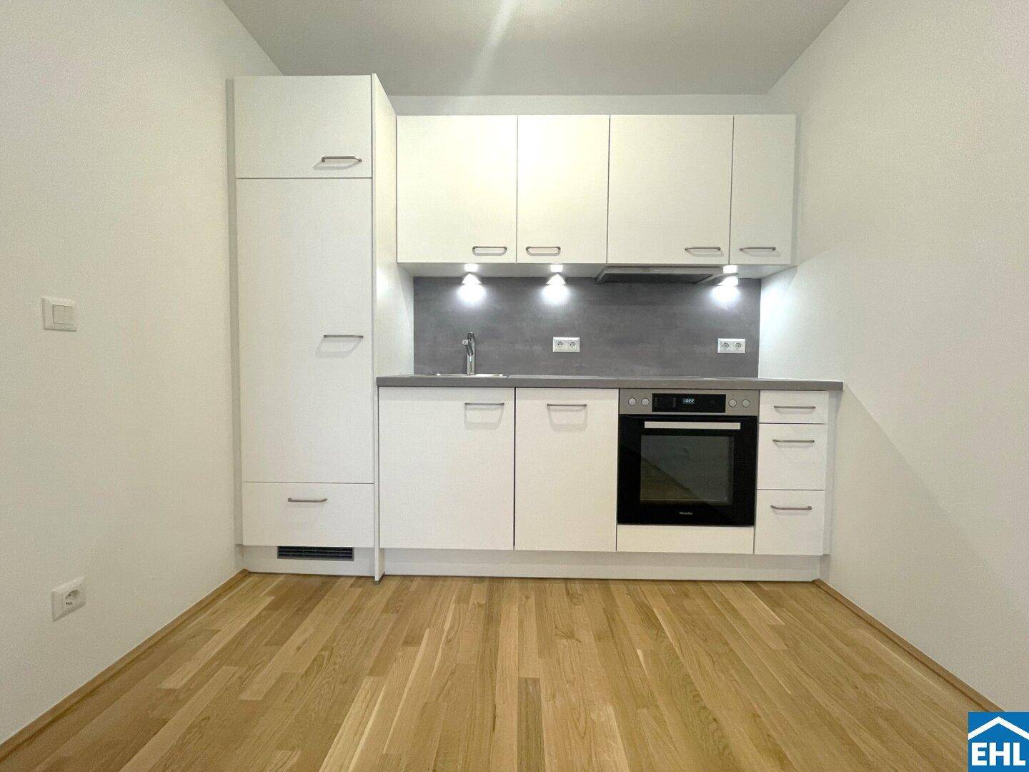 Moderne, kompakte Küchenzeile mit weißen Schränken, integriertem Backofen und viel Stauraum.