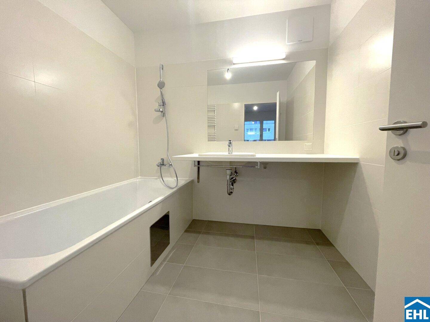 Modernes Badezimmer mit Badewanne, großem Waschtisch und hellen Fliesen, in neuwertigem Zustand.