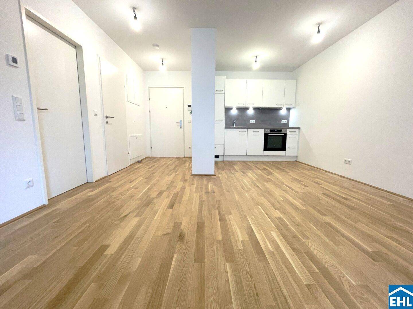 Offener Wohnbereich mit integrierter Küchenzeile und hellem Parkettboden in einem modernen Apartment.