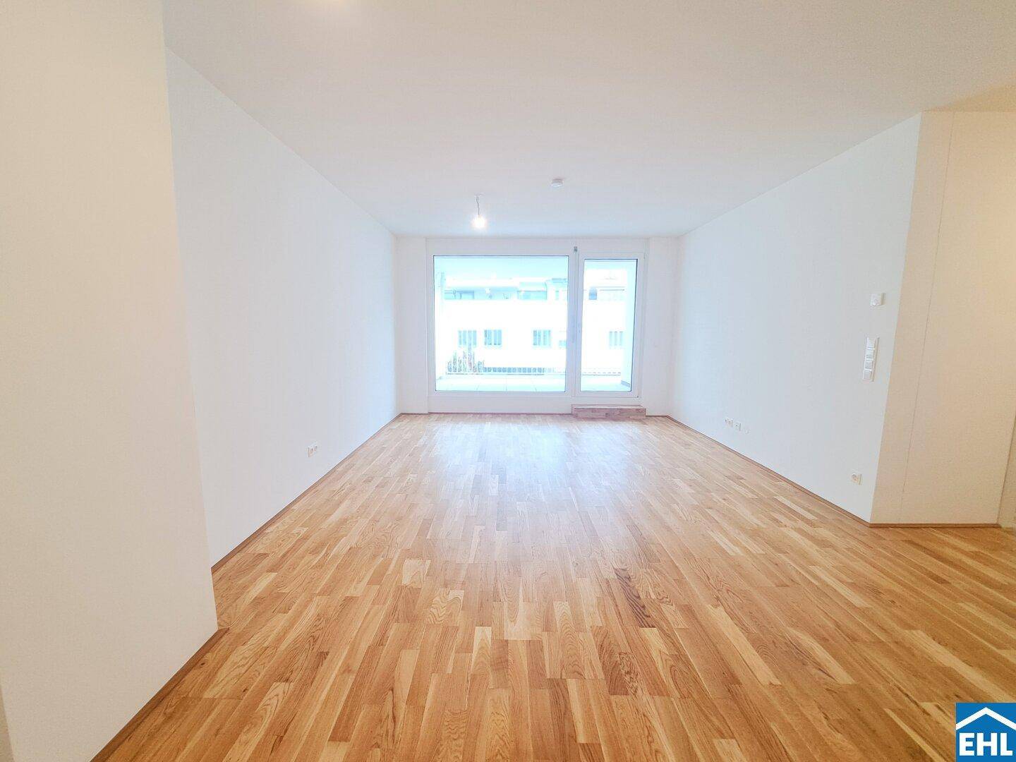 Lichtdurchfluteter Raum mit breiter Fensterfront und elegantem Parkettboden, ideal für offenes Wohnen.
