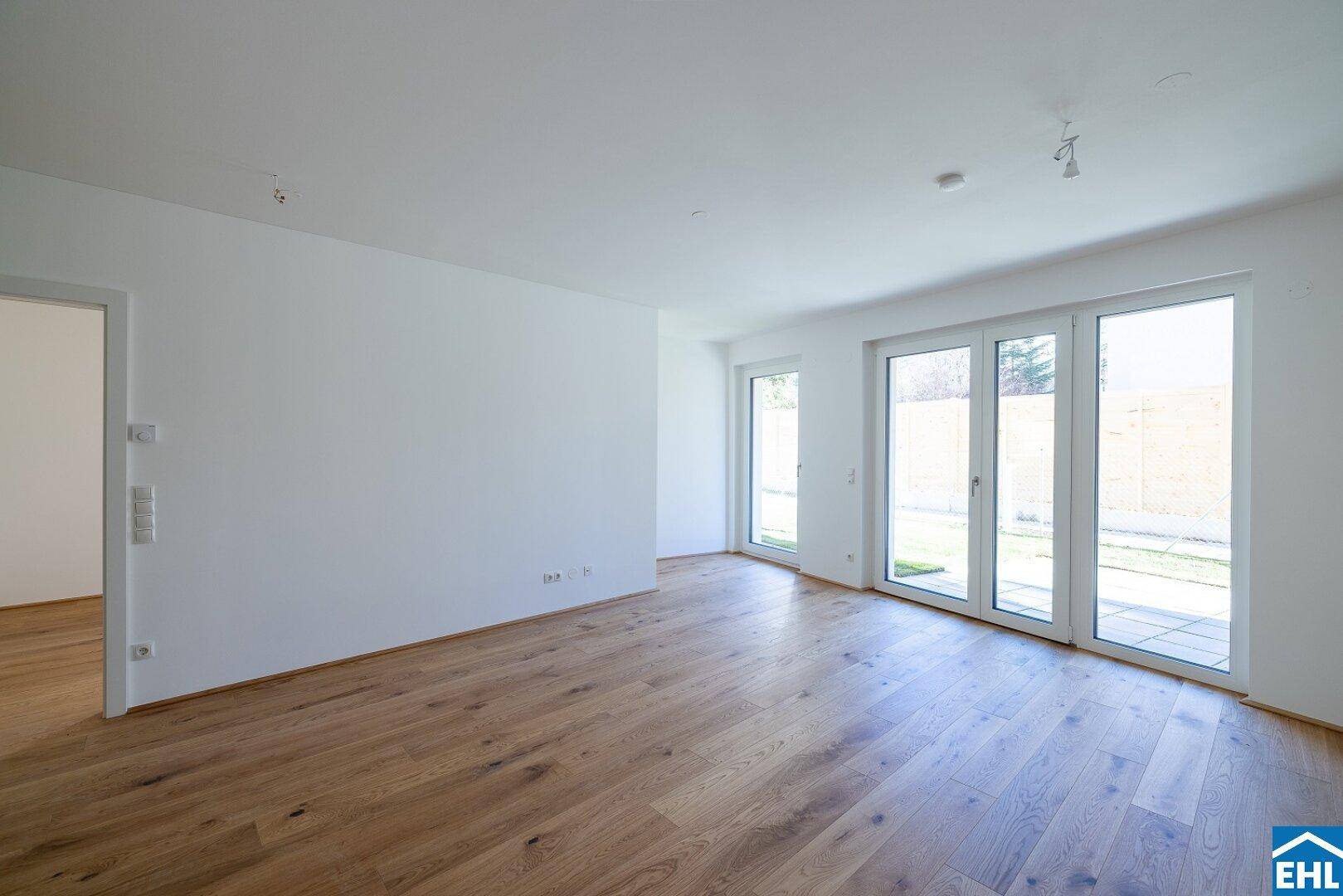 Heller, unmöblierter Raum mit Holzboden und großen Fenstertüren, bereit zur individuellen Gestaltung.