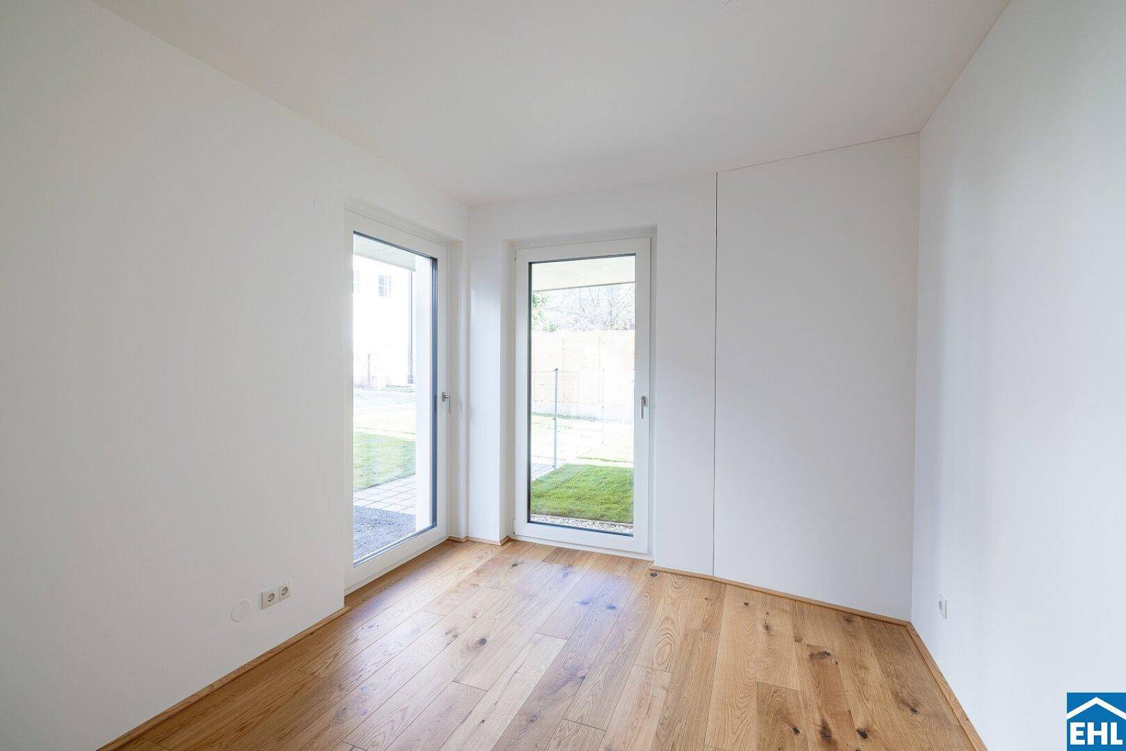 Kleinerer, heller Raum mit Holzboden und zwei Fenstertüren zum Außenbereich.