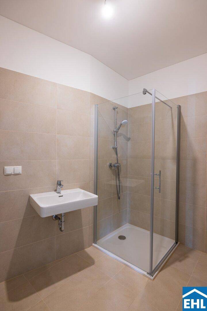 Helles Badezimmer mit Duschkabine, Einzelwaschbecken und neutralen beigefarbenen Wandfliesen.