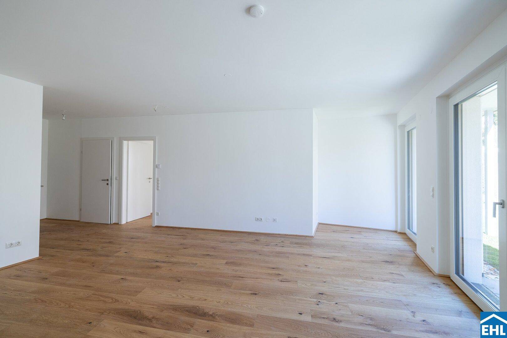 Geräumiger, leerer Raum mit Holzboden, großen Fenstern und Zugang zu weiteren Zimmern.